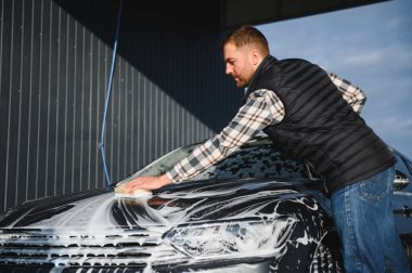 Süngerli bir işçi arabayı köpükle yıkar. Araba yıkama ve araba bakımı.