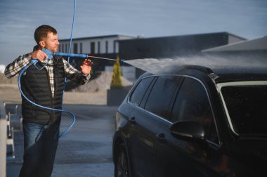 Adam yüksek basınçlı çamaşır makinesinden çıkan suyla araba yıkıyor..