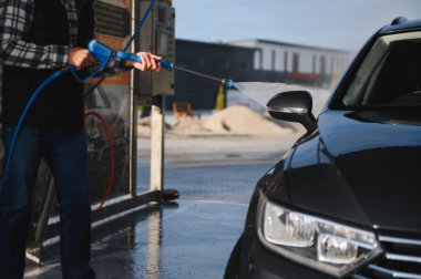 Bir adam arabasını tazyikli suyla yıkama makinesinde yıkıyor..