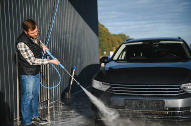 Adam yüksek basınçlı çamaşır makinesinden çıkan suyla araba yıkıyor..