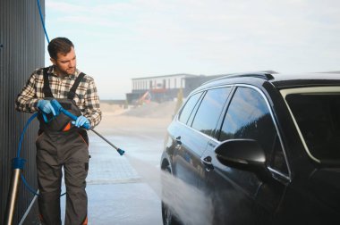 Üniformalı bir işçi ön taraftaki servis istasyonunu yıkıyor. Araba yıkama istasyonu..