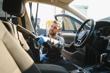 Araba yıkama ve araba yıkama konsepti. Genç bir adam, oto yıkama işçisi, koruyucu lastik eldiven giyiyor, arabanın içini temizliyor..