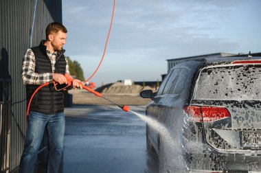 Bir adam arabayı yıkarken köpüğü yıkar. Bir araç araba yıkama sırasında sabunlu köpüğe bulanır, lastikleri, tekerlekleri, kaputu ve arabanın tüm dış kısmını kaplar. self-servis araba yıkama