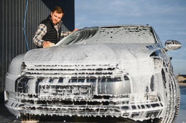 Süngerli bir işçi arabayı köpükle yıkar. Araba yıkama ve araba bakımı.