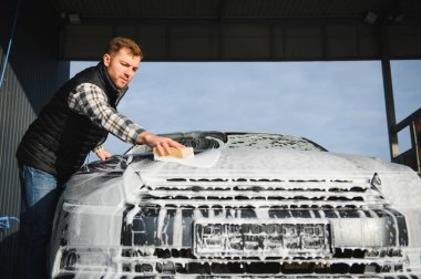 Bir adam oto yıkamada bir arabayı süngerle yıkar..