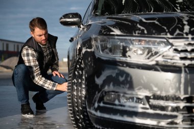 Bir adam oto yıkamada bir arabayı süngerle yıkar..