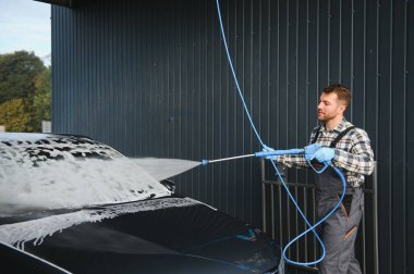 Araba yıkama uzmanı arabayı yıkamak için basınç makinesini kullanıyor..