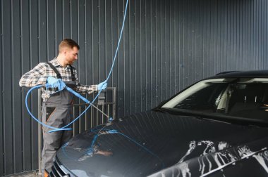 Araba yıkama uzmanı arabayı yıkamak için basınç makinesini kullanıyor..