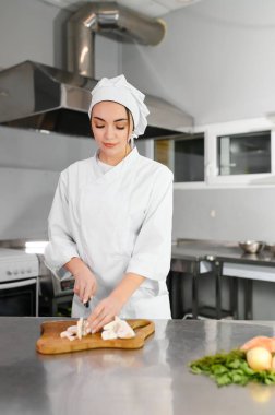 Genç, güzel, gülümseyen kadın şef mutfakta beyaz takım elbise giyiyor. Bulanık arkaplan.