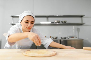 Kadın şef pizza üzerine peynir serper, restoran mutfağı....