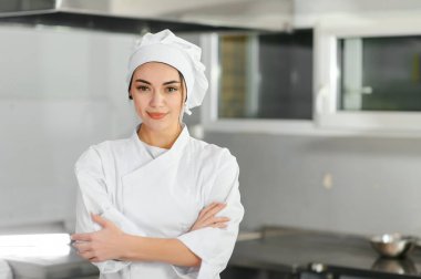 Genç, güzel, gülümseyen kadın şef mutfakta beyaz takım elbise giyiyor. Bulanık arkaplan.