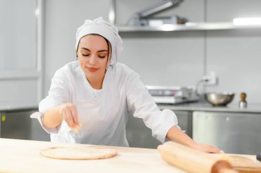 Güzel bayan şef restoran mutfağında peynirli pizza pişiriyor. Yarı bitmiş ürünler ve donmuş gıda kavramı..