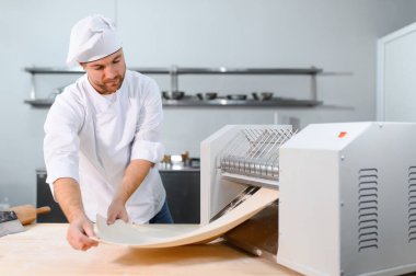 Geleneksel İtalyan yemekleri. Mutfaktaki makarna makinesinde hamuru yuvarlayan yakışıklı şefin yan görünüşü.