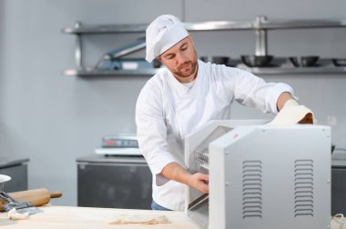 Geleneksel İtalyan yemekleri. Mutfaktaki makarna makinesinde hamuru yuvarlayan yakışıklı şefin yan görünüşü.