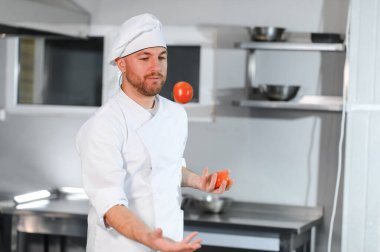 Neşeli ve komik erkek aşçı restoran mutfağında sebzelerle hokkabazlık yapıyor..