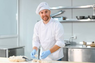 Genç aşçı, profesyonel mutfakta hamur yoğurur. Yarı bitmiş ürünler kavramı.