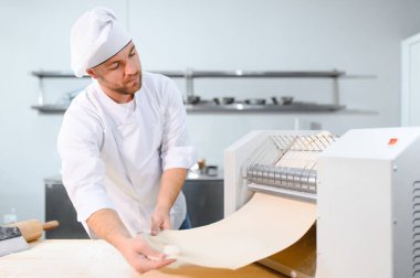 Geleneksel İtalyan yemekleri. Mutfaktaki makarna makinesinde hamuru yuvarlayan yakışıklı şefin yan görünüşü.