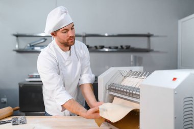Geleneksel İtalyan yemekleri. Mutfaktaki makarna makinesinde hamuru yuvarlayan yakışıklı şefin yan görünüşü.