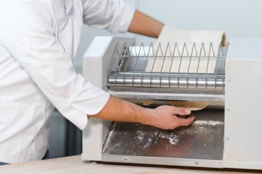 Geleneksel İtalyan yemekleri. Mutfaktaki makarna makinesinde hamuru yuvarlayan yakışıklı şefin yan görünüşü.