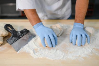 Genç aşçı, profesyonel mutfakta hamur yoğurur. Yarı bitmiş ürünler kavramı.