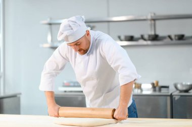 Genç aşçı, profesyonel mutfakta hamur yoğurur. Yarı bitmiş ürünler kavramı.