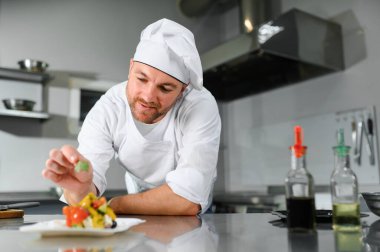 Yemek pişirme, meslek ve insan konsepti. Mutfak masasında salata tabağıyla mutlu aşçı erkek..
