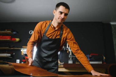 İşyerindeki malzemeyi kontrol eden profesyonel bir zanaatkar, deri giysiler, ayakkabılar ve aksesuarlar için hakiki deri rulo kalitesini kontrol eder..