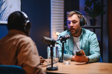 Podcaster 'lar stüdyodaki çevrimiçi dinleyicilerle keyifli sohbetler yapıyorlar, çeşitli konuları kapsıyorlar..