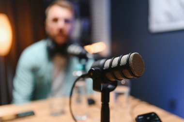 Arka plandaki profesyonel mikrofon ve podcast sunucusuna odaklan.