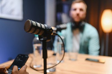 Arka plandaki profesyonel mikrofon ve podcast sunucusuna odaklan.