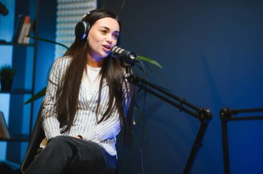 Kulaklıklı kadın podcaster mikrofon kullanarak, gülümseyerek, kayıt yaparak ve stüdyoda ses yayını yaparak erkek konukla röportaj yapıyor. İçerik oluşturucu, günlükler.