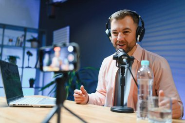 Stüdyoda podcast yaparken gülümseyen adam.