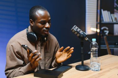 Siyah vlogger stüdyoda akıllı telefondan podcast çekiyor. Afro-amerikan etkileyicisi telefon ekranına bakıyor ve iyi haberleri seyircilere ve abonelere veriyor. Neşeli blogcu