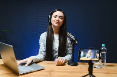 Kameraya bakan kadın vlogger etkileyicisi, genç kadın blogger hayranlarını selamlıyor ve akıllı telefona bakarak konuşuyor, çevrimiçi video konferansına katılıyor.