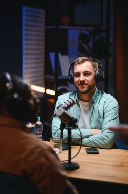 Adam podcaster etkili blogcu gülümseyerek stüdyoda kulaklık kullanarak canlı yayın yapıyor. Erkek radyo sunucusu podcast veya röportaj yapıyor.