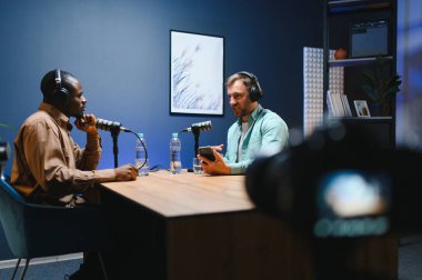 Canlı yayın tartışması ile çevrimiçi içerik oluşturarak, podcast bölümünü birlikte yayınlamak üzere sunucu ve misafir toplantısını göster. Vlog kaydedicisi sohbet kaydetmek için profesyonel ekipman kullanan bir adamla konuşuyor.