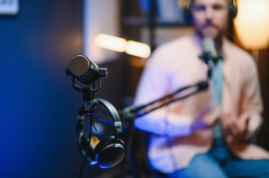 Adam podcaster etkili blogcu gülümseyerek stüdyoda kulaklık, dizüstü bilgisayar ve kulaklık kullanarak canlı yayın yapıyor. Erkek radyo sunucusu podcast veya röportaj yapıyor