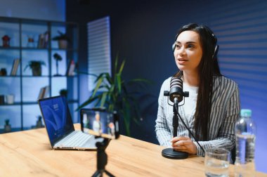Kameraya bakan kadın vlogger etkileyicisi, genç kadın blogger hayranlarını selamlıyor ve akıllı telefona bakarak konuşuyor, çevrimiçi video konferansına katılıyor.