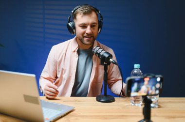 Adam podcaster etkili blogcu gülümseyerek stüdyoda kulaklık kullanarak canlı yayın yapıyor. Erkek radyo sunucusu podcast veya röportaj yapıyor.