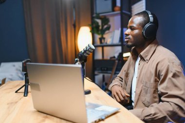 Genç Afrikalı Amerikalı erkek video blogcusu profesyonel mikrofonla stüdyoda video blogu kaydediyor.