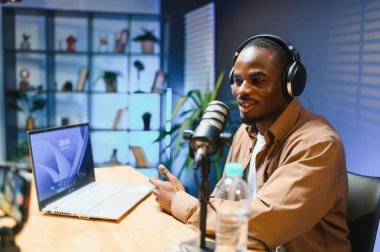 Siyah vlogger stüdyoda akıllı telefondan podcast çekiyor. Afro-amerikan etkileyicisi telefon ekranına bakıyor ve iyi haberleri seyircilere ve abonelere veriyor. Neşeli blogcu