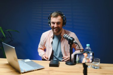 Stüdyoda podcast yaparken gülümseyen adam.