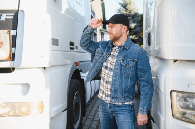 Nakliye aracı. Yakışıklı bir kamyon şoförü otoparkta bir kamyonun arkasında duruyor..
