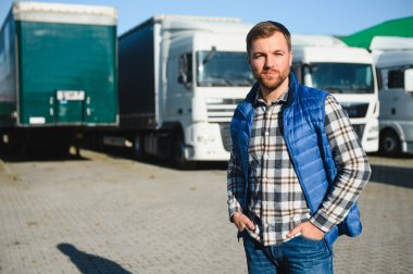 Nakliye aracı. Yakışıklı bir kamyon şoförü otoparkta bir kamyonun arkasında duruyor..