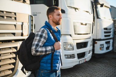 Nakliye aracı. Yakışıklı bir kamyon şoförü otoparkta bir kamyonun arkasında duruyor..