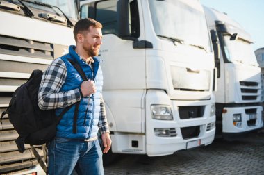 Nakliye aracı. Yakışıklı bir kamyon şoförü otoparkta bir kamyonun arkasında duruyor..