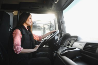 Büyük bir kamyonda oturan, kameraya bakıp gülümseyen güzel, genç kadın kamyon şoförünün portresi. Aracın içinde. İnsanlar ve ulaşım kavramı.