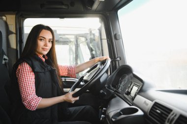 Büyük bir kamyonda oturan, kameraya bakıp gülümseyen güzel, genç kadın kamyon şoförünün portresi. Aracın içinde. İnsanlar ve ulaşım kavramı.