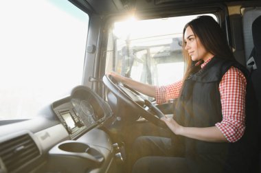 Büyük bir kamyonda oturan, kameraya bakıp gülümseyen güzel, genç kadın kamyon şoförünün portresi. Aracın içinde. İnsanlar ve ulaşım kavramı.