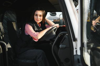 Büyük bir kamyonda oturan, kameraya bakıp gülümseyen güzel, genç kadın kamyon şoförünün portresi. Aracın içinde. İnsanlar ve ulaşım kavramı.